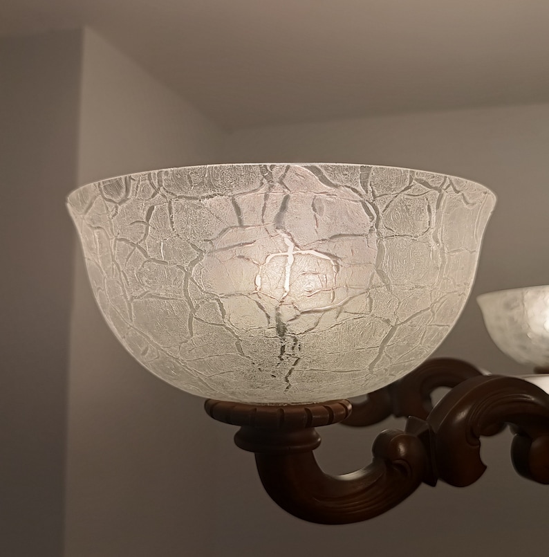 May include: A close-up of a frosted glass lampshade with a textured surface. The lampshade is attached to a brown metal lamp fixture.