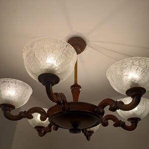 May include: A wooden chandelier with five frosted glass shades. The shades have a textured, crackled finish and are lit from within.