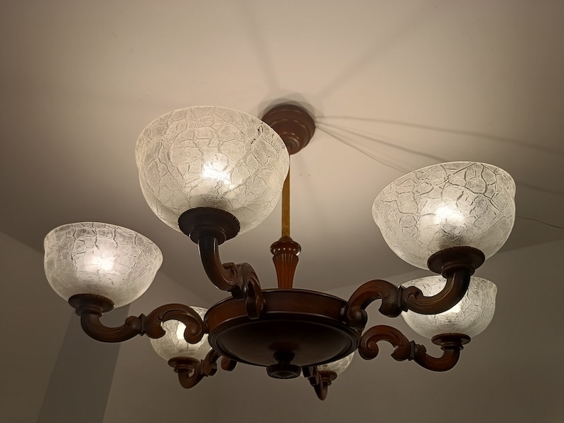 May include: A wooden chandelier with five frosted glass shades. The shades have a textured, crackled finish and are lit from within.