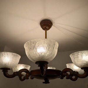 May include: A five-light chandelier with a dark brown wooden frame and clear glass shades with a textured surface. The shades are shaped like bowls and have a frosted appearance.