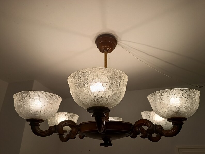 May include: A five-light chandelier with a dark brown wooden frame and clear glass shades with a textured surface. The shades are shaped like bowls and have a frosted appearance.