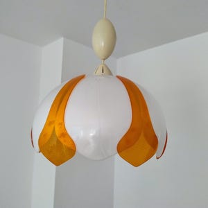 Peut inclure: Un luminaire suspendu vintage avec un abat-jour blanc en forme de fleur et des accents orange. La lumi&egrave;re est suspendue &agrave; un luminaire ovale de couleur cr&egrave;me. Le luminaire est suspendu &agrave; un cordon fin de couleur cr&egrave;me.