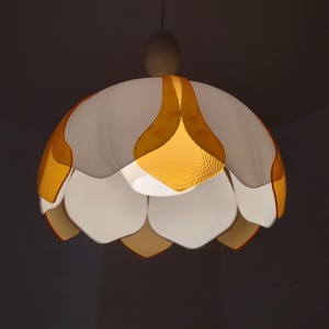 Peut inclure: Un luminaire suspendu blanc et dor&eacute; avec un design floral. La lampe a un abat-jour blanc en forme de p&eacute;tale avec des accents dor&eacute;s et une finition textur&eacute;e. Le luminaire est suspendu &agrave; un cordon blanc.