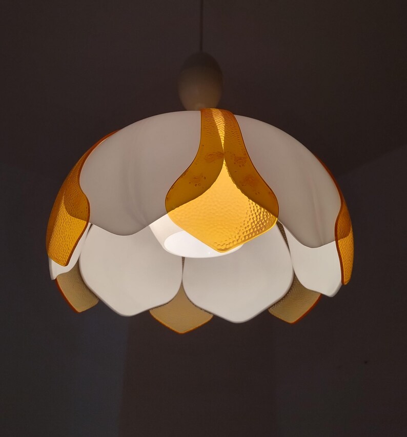 Peut inclure: Un luminaire suspendu blanc et dor&eacute; avec un design floral. La lampe a un abat-jour blanc en forme de p&eacute;tale avec des accents dor&eacute;s et une finition textur&eacute;e. Le luminaire est suspendu &agrave; un cordon blanc.