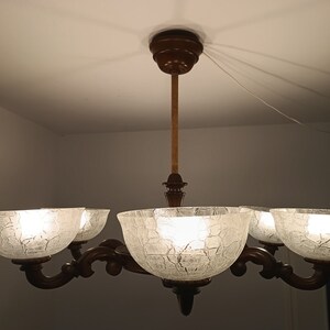 May include: A five-light chandelier with a brown wooden frame and clear glass shades. The shades have a textured, crackled glass design.