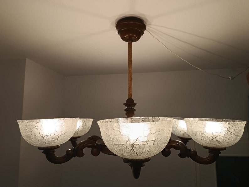 May include: A five-light chandelier with a brown wooden frame and clear glass shades. The shades have a textured, crackled glass design.