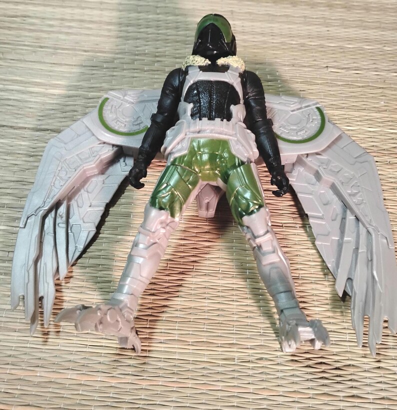 Pu&ograve; includere: Action figure di Vulture con ali articolate. La figura presenta un elmetto verde e nero, un busto nero e bianco e gambe verdi e bianche. Le ali sono grigie con dettagli verdi. La figura &egrave; in posa con le gambe divaricate.