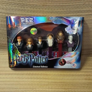 May include: A Harry Potter Limited Edition PEZ Collector's Series gift set featuring six character dispensers including Harry, Hermione, Ron, Dumbledore, Hagrid, and Voldemort, packaged in a holographic box with a golden snitch and owl graphic.