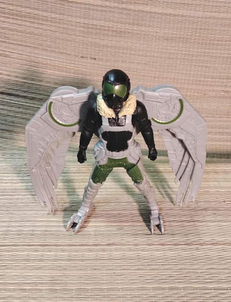Pu&ograve; includere: Una action figure di Vulture, con un casco nero e visiera verde, una tuta nera e verde e grandi ali grigie con dettagli verdi. La figura ha un colletto di pelliccia marrone e un'armatura per le gambe dettagliata.