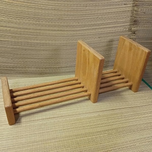 May include: A light brown wooden rack featuring a series of horizontal dowels connected by three vertical rectangular panels. The structure is designed with a slatted base and two upright dividers, creating two distinct sections for storage.