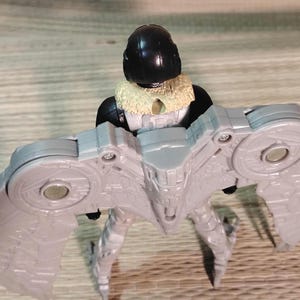 Pu&ograve; includere: Action figure grigia di un personaggio con elmetto nero, colletto beige e apparato alare grigio. La figura &egrave; in piedi con le ali spiegate. La figura &egrave; un giocattolo.