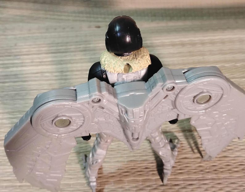 Pu&ograve; includere: Action figure grigia di un personaggio con elmetto nero, colletto beige e apparato alare grigio. La figura &egrave; in piedi con le ali spiegate. La figura &egrave; un giocattolo.
