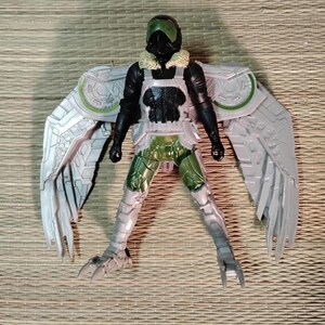 Pu&ograve; includere: Action figure di Vulture con ali articolate. La figura presenta un casco nero e verde, una tuta nera e un'armatura argentata e verde. Le ali sono dettagliate con un design a forma di piuma. La figura &egrave; posata su una superficie tessuta.