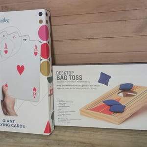 Peut inclure: Deux jeux de société : un jeu de cartes géantes avec des cœurs rouges et un jeu de lancer de sacs de bureau avec un plateau en bois et des sacs de haricots bleus. La boîte de cartes a l'inscription "Giant Playing Cards" et la boîte de lancer de sacs a l'inscription "Desktop Bag Toss".