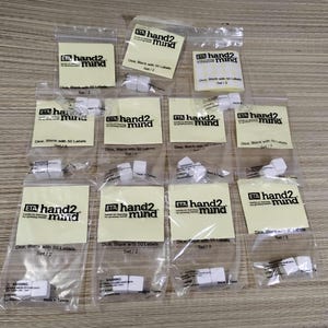 May include: A collection of clear plastic bags containing white dice with labels. Each label reads "hand2mind" and "Dice, Blank with 50 Labels Set/2". The dice are blank and ready for customization.