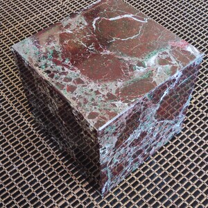 May include: A square, red and green marble coffee table with a polished finish. The table is sitting on a brown and black patterned rug.
