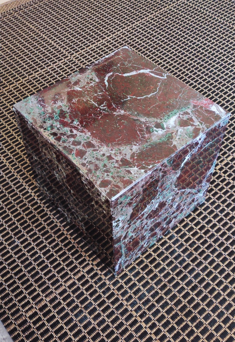 May include: A square, red and green marble coffee table with a polished finish. The table is sitting on a brown and black patterned rug.