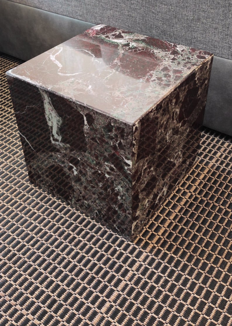 May include: A square, dark brown marble end table with a polished surface. The table has a unique pattern of white and green veins throughout the marble.