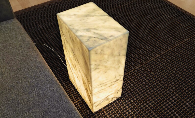 May include: A white marble cube lamp with a warm, glowing light. The lamp is sitting on a black and brown patterned rug.