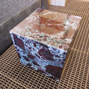 May include: A square, red and green marble end table with a polished surface.