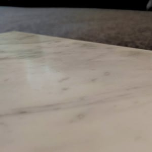 May include: A close-up of a white marble surface with subtle veining. The surface is smooth and polished, reflecting light.