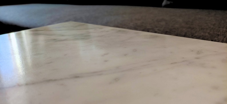 May include: A close-up of a white marble surface with subtle veining. The surface is smooth and polished, reflecting light.