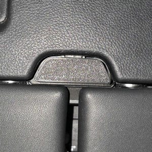 Puede incluir: Primer plano del interior de un coche negro. La imagen muestra superficies de cuero texturizado, centrándose en una consola central con un panel rectangular texturizado y detalles circundantes.