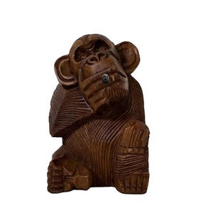 May include: A brown wooden carving of a seated monkey with its hand raised to its mouth. The figure features detailed linear textures across its body, prominent ears, and a small circular inlay on its face, capturing a contemplative pose.