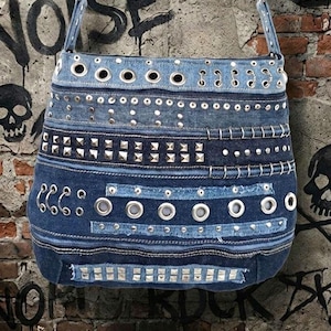 May include: A denim shoulder bag with a patchwork design. The bag features various shades of blue denim, embellished with silver grommets, studs, and rivets. The bag has a long strap and a rounded shape, perfect for carrying essentials.