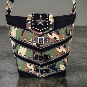 May include: A black and camouflage print shoulder bag with a star-shaped embellishment on the flap. The bag features multiple zippers, silver studs, and buckle details. The bag has a black strap and a black base.