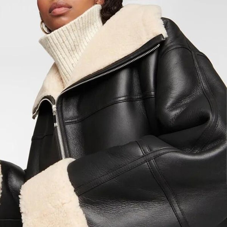 May include: A black leather jacket with a shearling collar and cuffs. The jacket has a zipper closure and a stand-up collar.