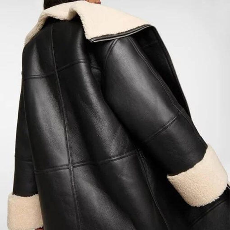 May include: A black leather shearling jacket with a white shearling collar and cuffs. The jacket has a classic bomber style with a zipper closure and flap pockets.