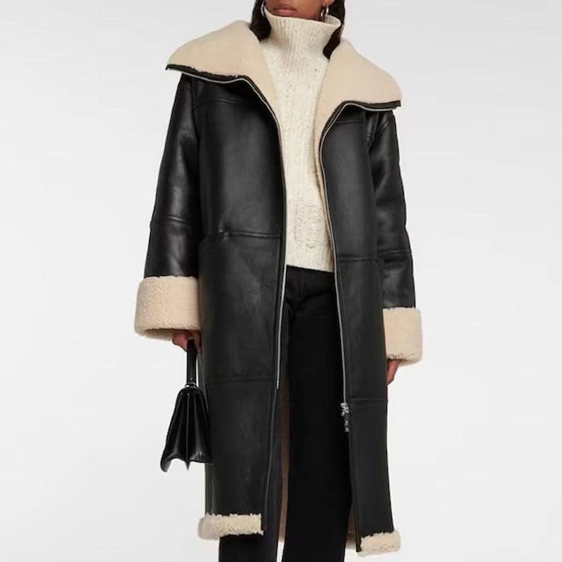 May include: A long black faux leather coat with a shearling collar and cuffs. The coat has a zipper closure and a relaxed fit.