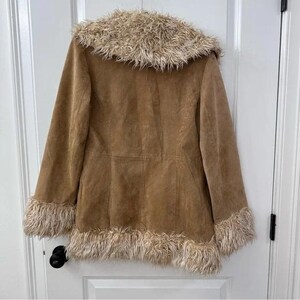 May include: A tan suede coat with a faux fur collar and cuffs. The coat has a button closure and a tailored fit. The faux fur trim is a light brown colour. The coat is a vintage style.