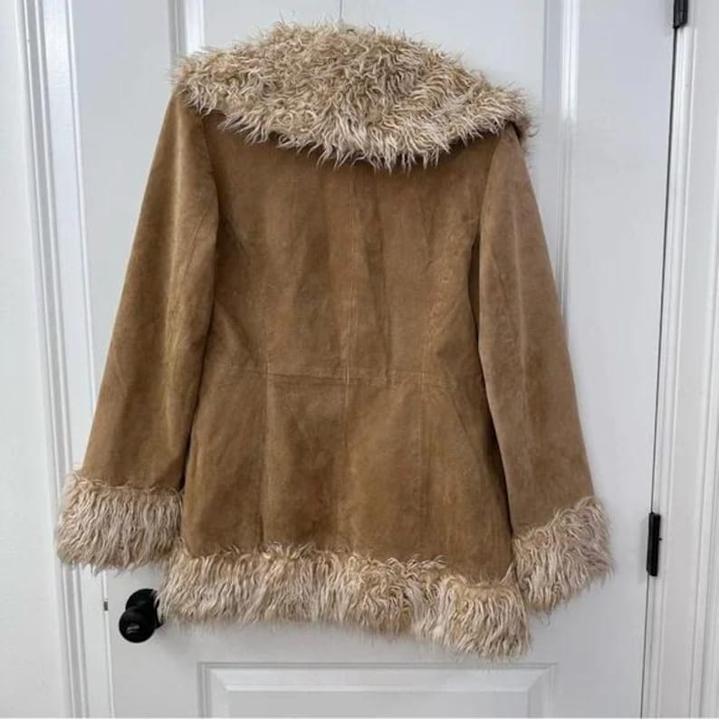 May include: A tan suede coat with a faux fur collar and cuffs. The coat has a button closure and a tailored fit. The faux fur trim is a light brown colour. The coat is a vintage style.
