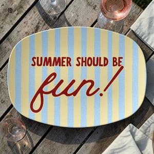 May include: An oblong serving platter with a yellow and light blue striped pattern. The platter has the text "SUMMER SHOULD BE fun!" in a red script font. The platter is on a wooden table with glasses of wine.