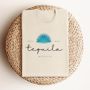 May include: A beige t-shirt with a blue agave plant graphic and the text "EST. 1850 tequila MEXICO".