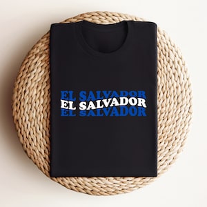 May include: Black t-shirt with the text "EL SALVADOR" repeated three times in blue and white letters.