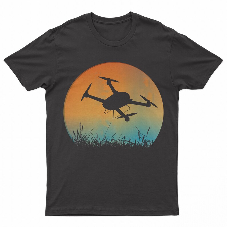 May include: A black t-shirt with a silhouette of a drone flying in front of a sunset. The sunset is a gradient of orange, yellow, and blue.