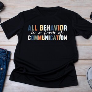May include: Black t-shirt with the text "ALL BEHAVIOR is a form of COMMUNICATION" in colorful letters.