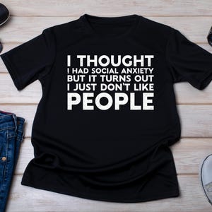May include: Black t-shirt with white text that reads "I thought I had social anxiety but it turns out I just don't like people."
