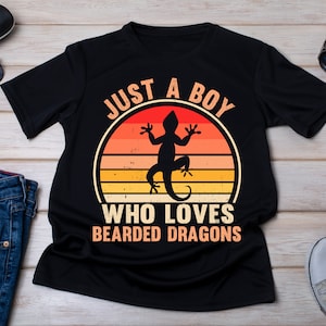 Może przedstawiać: Czarny T-shirt z grafiką w stylu retro przedstawiającą jaszczurkę i tekstem "Just a Boy Who Loves Bearded Dragons".