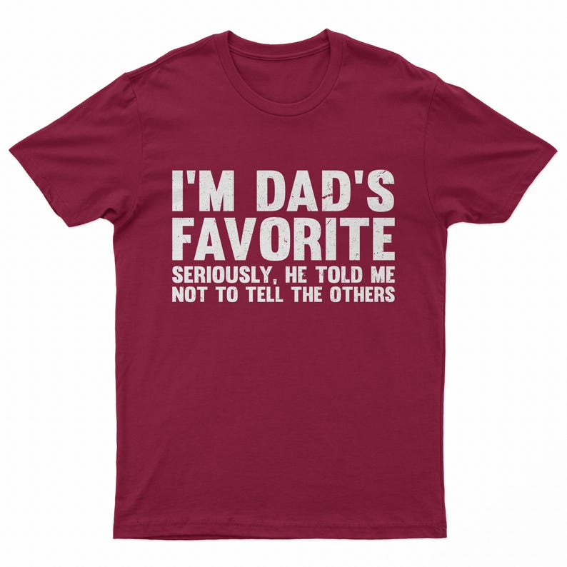 May include: A maroon t-shirt with white text that reads "I'M DAD'S FAVORITE" in a bold font. Below, in a smaller font, it says "SERIOUSLY, HE TOLD ME NOT TO TELL THE OTHERS."