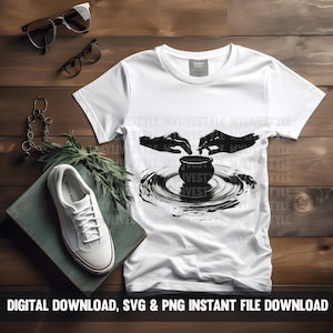 May include: A white t-shirt with a black graphic of two hands shaping a pot on a pottery wheel. The graphic is in a minimalist style with a black and white color scheme.