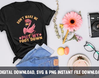 May include: A black t-shirt with the text "Don't make me put my foot down" in white and orange. A pink flamingo with a flower crown is standing on one leg. The shirt is on a blue denim background.