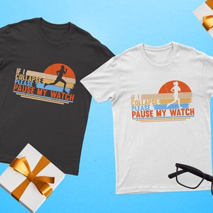 May include: Two t-shirts with a retro-style graphic of a runner and the text "If I collapse please pause my watch". One shirt is black and the other is white.