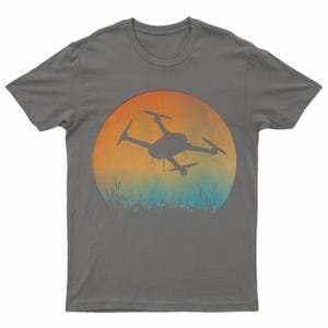 May include: A dark gray t-shirt with a graphic of a drone flying in front of a sunset. The sunset is a gradient of orange, yellow, and blue.