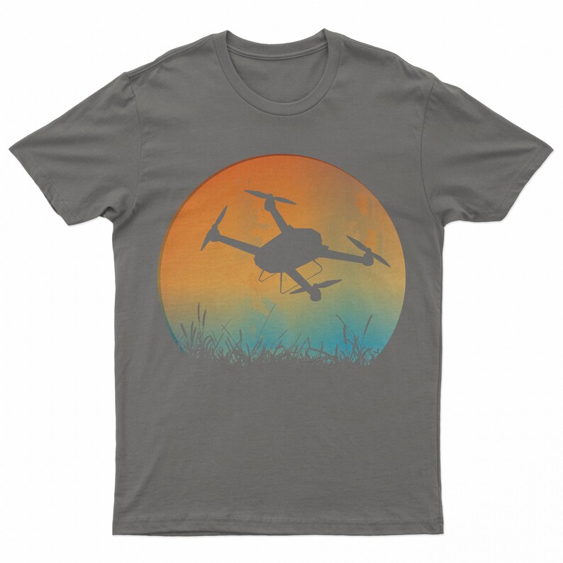 May include: A dark gray t-shirt with a graphic of a drone flying in front of a sunset. The sunset is a gradient of orange, yellow, and blue.