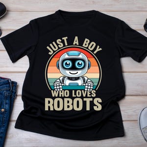 Op de afbeelding: Zwart t-shirt met een robotafbeelding. De robot is wit en blauw, tegen een retro zonsondergang. Tekst luidt "JUST A BOY WHO LOVES ROBOTS". Accessoires zijn zonnebril, horloge en jeans.