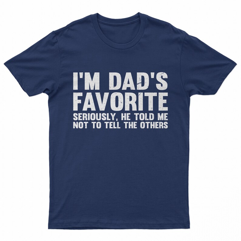 May include: Navy blue t-shirt with white text that reads "I'M DAD'S FAVORITE" in large capital letters. Below, smaller text says "SERIOUSLY, HE TOLD ME NOT TO TELL THE OTHERS". The shirt is a casual wear item.